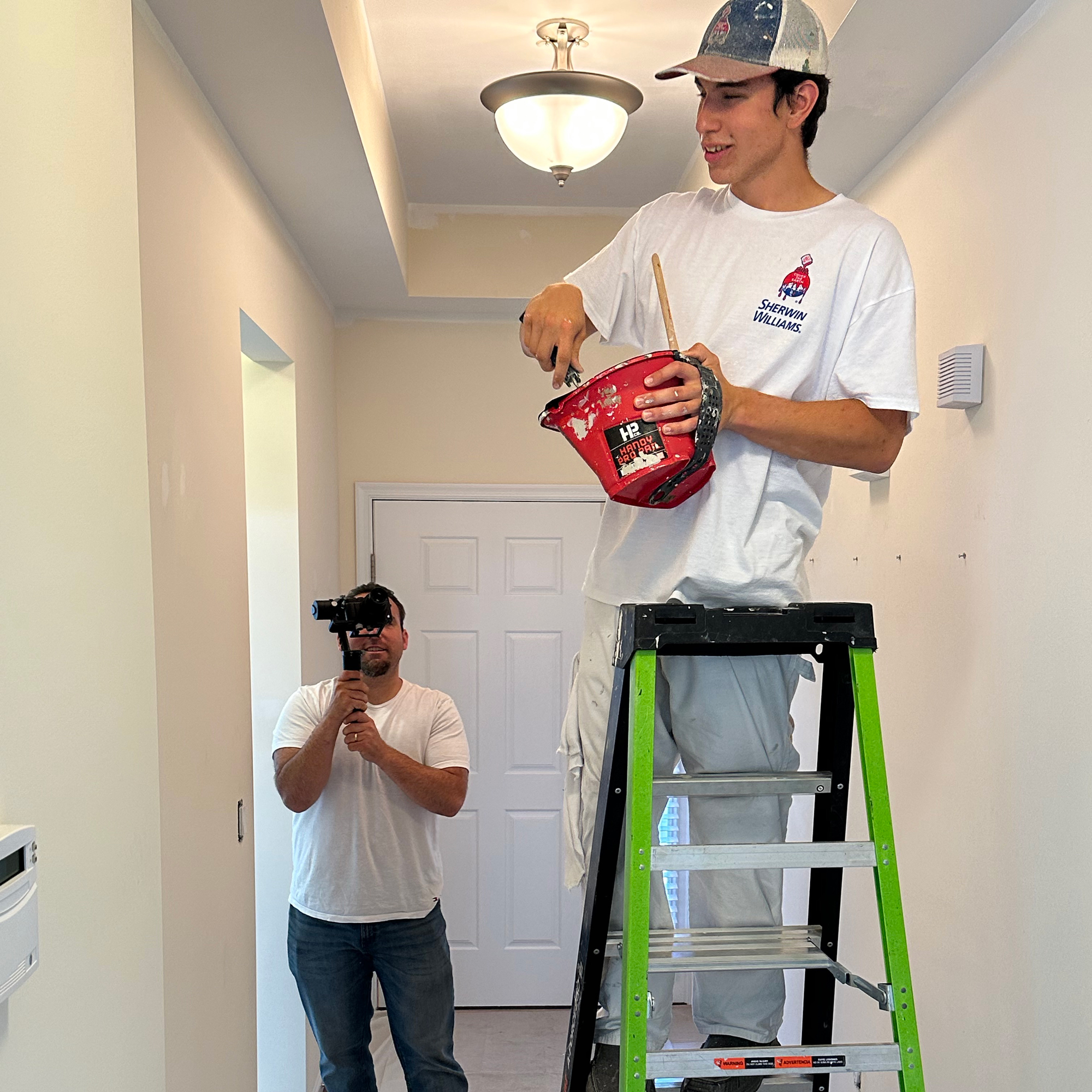 Matt makes painter on ladder smile shooting All Business Video in white t-shirt